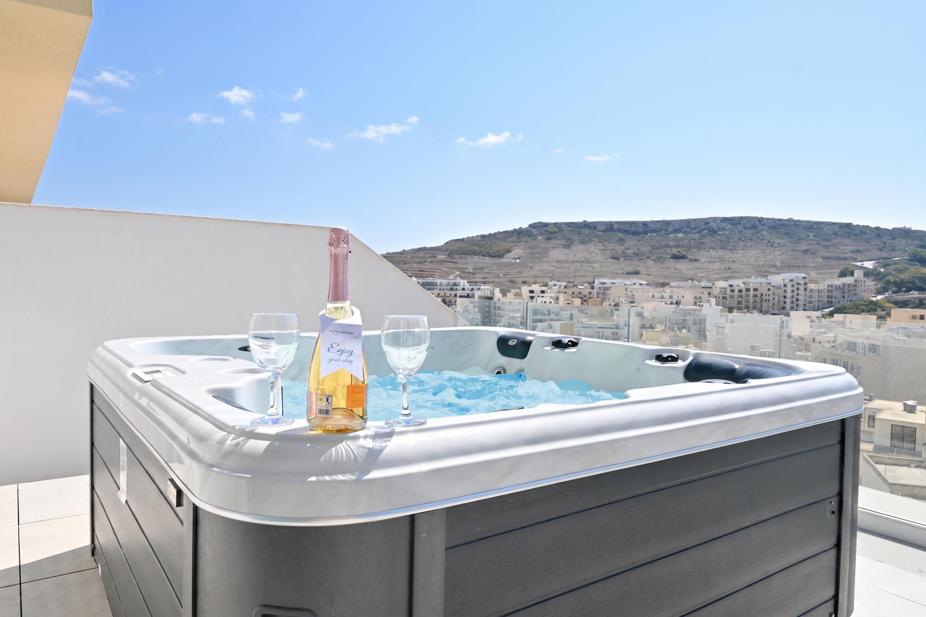 Ein Whirlpool mit einer Champagnerflasche und Gläsern auf einem Balkon mit Blick auf die Stadt.