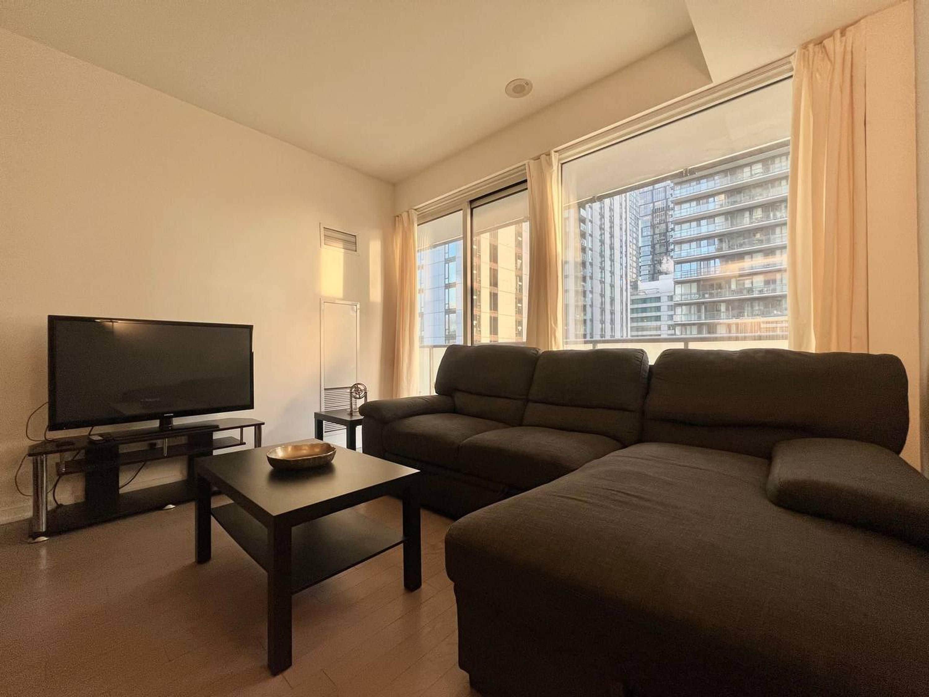 A living room with a flat-screen TV, a dark sofa, a coffee table, and a window with curtains.