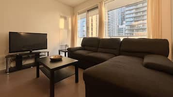 A living room with a flat-screen TV, a dark sofa, a coffee table, and a window with curtains.