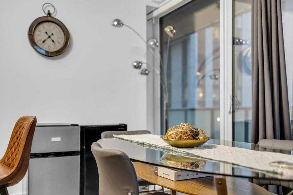 A modern kitchen with a dining table, chairs, a clock, and a window with curtains.