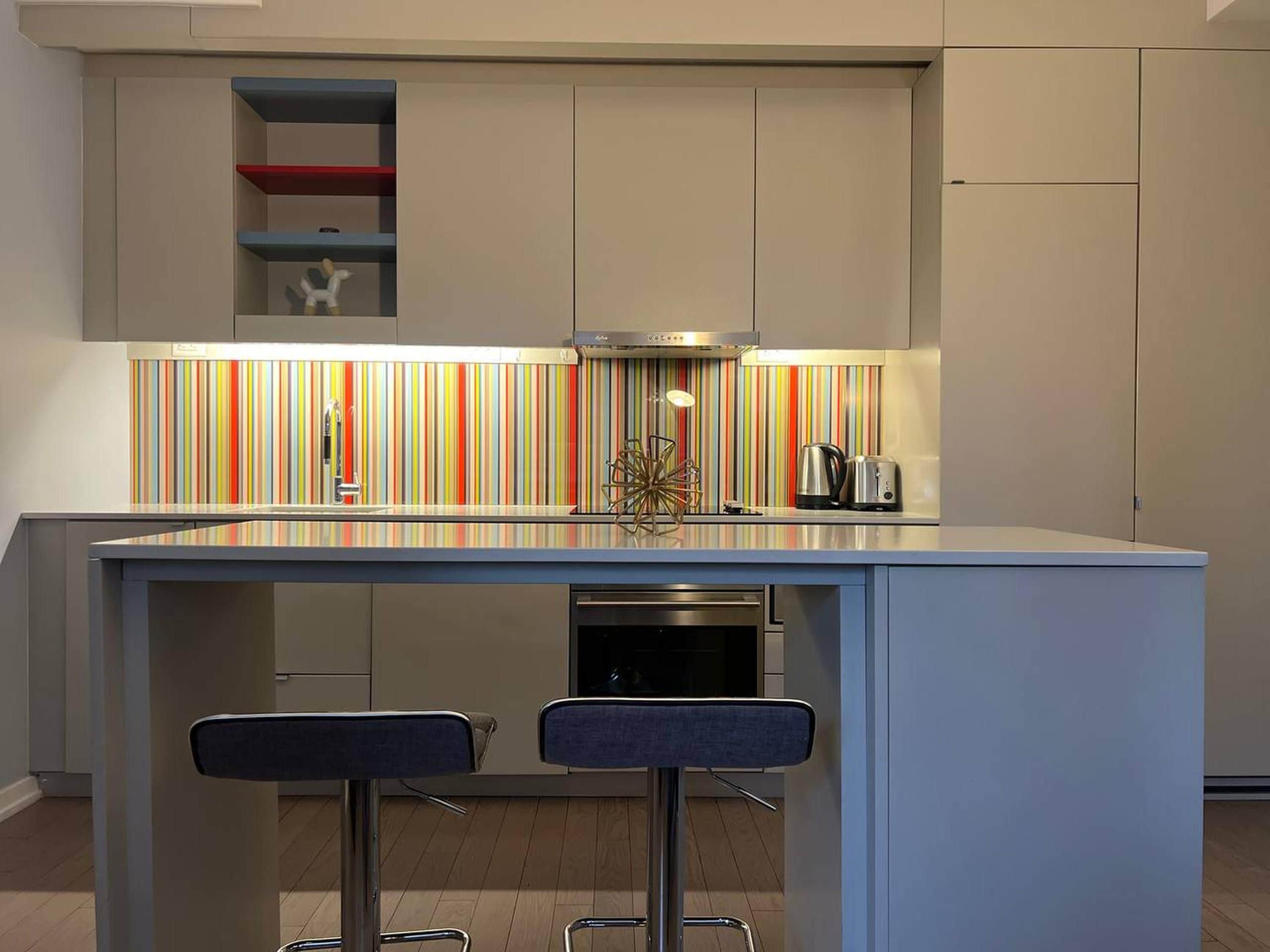A modern kitchen with a central island, bar stools, a colorful striped backsplash, and built-in appliances.