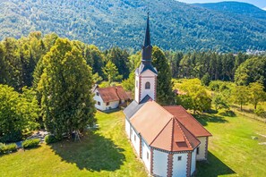 Une église dotée d’un clocher imposant, entourée d’une végétation luxuriante et située dans un paysage vallonné.
