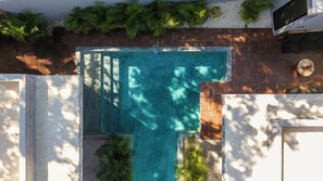 A swimming pool with a wooden deck surrounding it, a stone wall, and some greenery. - Casa Santo: Private Villa with Swim-up Suites, Courtyard Pool & Concierge (Tulum)
