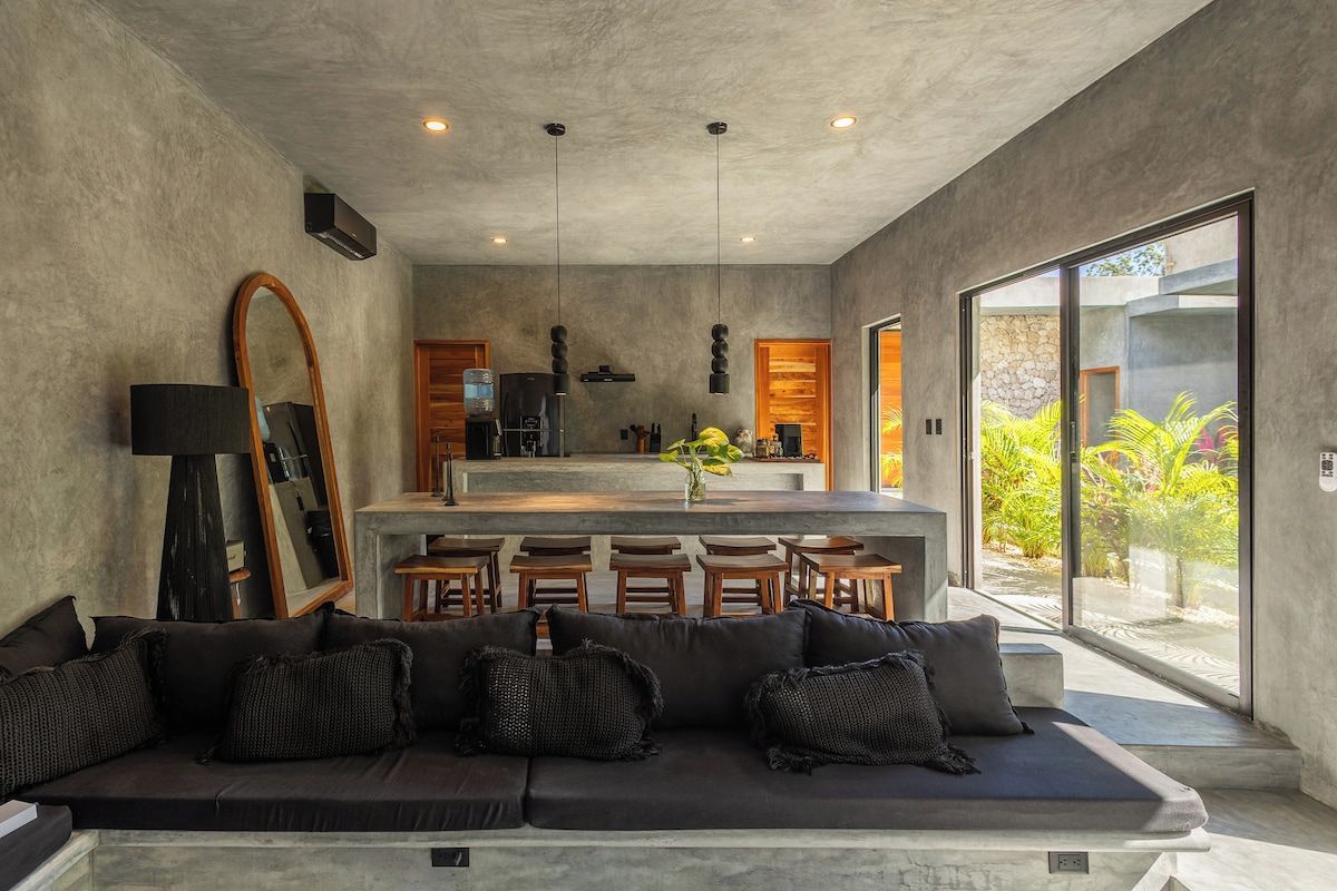 A modern interior with a sofa, a kitchen area, and large windows.