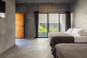 Un dormitorio con un amplio ventanal corredera que da a un balcón, una cama con ropa blanca y una puerta de madera.