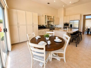 A modern kitchen with white cabinetry, a central island with stools, and a dining table set for four. - Palm Desert 4-Bedroom Retreat with a sparkling pool in the heart of Palm Desert (Palm Desert)