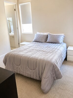 Une chambre à coucher comprenant un lit, une table de chevet, une commode et une porte donnant sur une salle de bain.