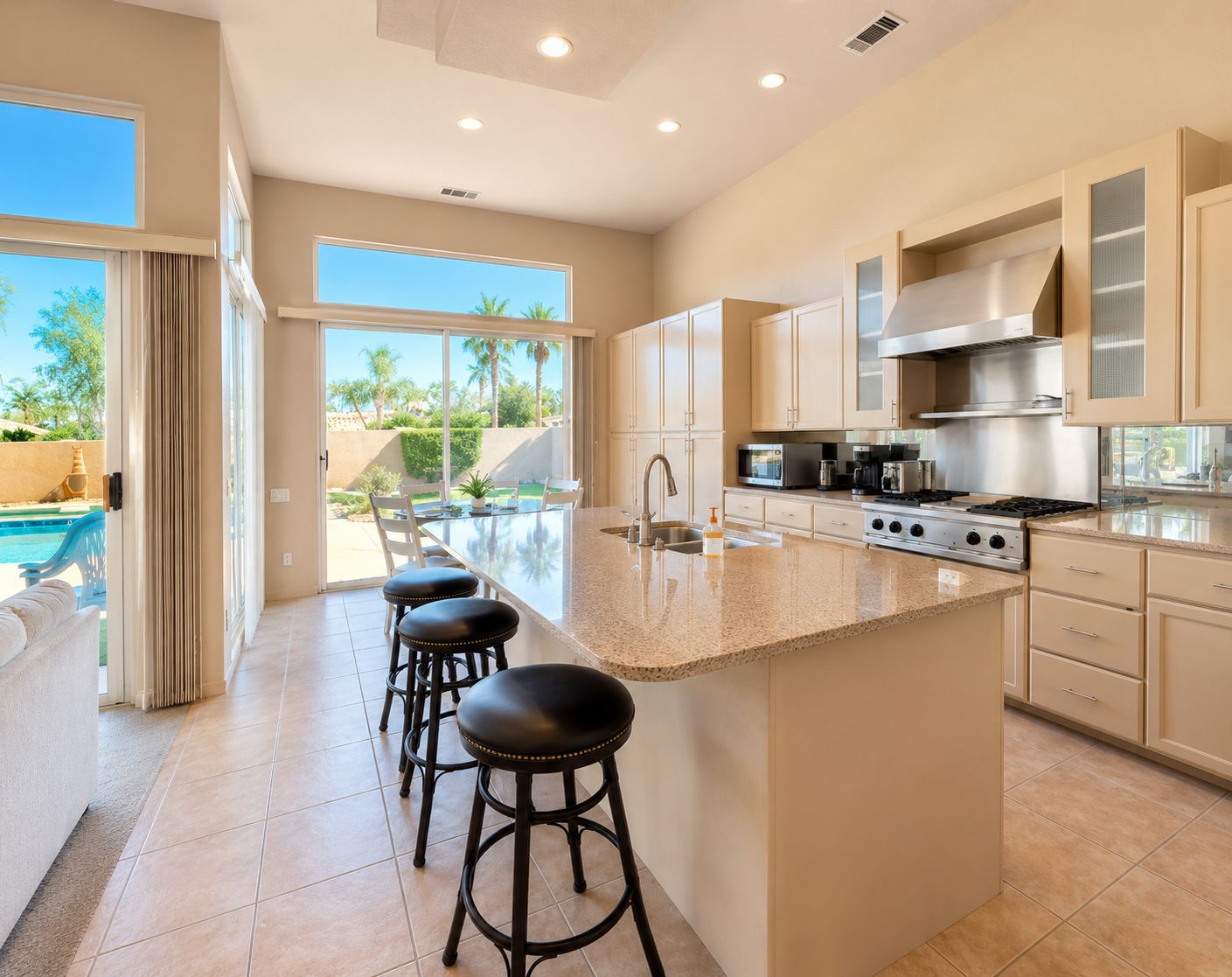 A modern kitchen with a large island, bar stools, and a view of a swimming pool.