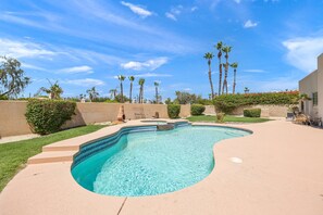 Piscina com design curvo, rodeada por um deck de concreto e um muro baixo com vegetação.