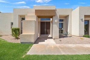 Une maison moderne à deux étages, dotée d’une façade symétrique, d’une entrée centrale avec une double porte et d’un petit patio agrémenté d’une plante en pot.