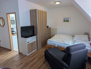 A bedroom with a bed, a TV on a stand, a wardrobe, and a small table. - Eulenhaus - FeWo OG (Cuxhaven)