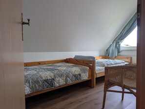 Ein Schlafzimmer mit zwei Holzbettgestellen übereinander, einem Korbstuhl und einem Fenster mit Vorhängen.