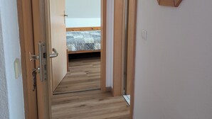 Un corridoio con pavimento in legno che conduce a una camera da letto con un letto e una finestra.