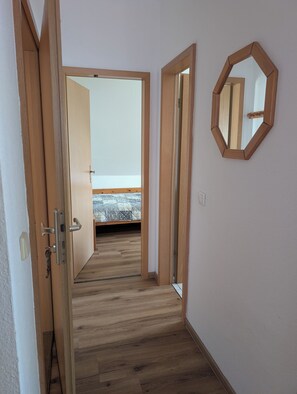A hallway with wooden flooring leading to a bedroom with a bed and a window. - Eulenhaus - FeWo OG (Cuxhaven)