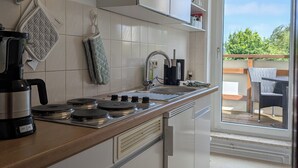 A modern kitchen with a gas stove, coffee maker, and a view to an outdoor patio. - Eulenhaus - FeWo OG (Cuxhaven)