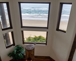 Una habitación con vistas a la playa a través de varias ventanas, un taburete de madera y una planta en maceta.