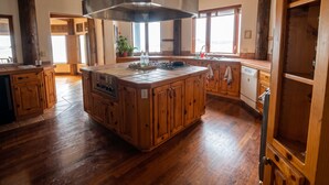 A spacious kitchen with a large island, wooden cabinetry, and a stainless steel range hood. - Brewer’s Bluff | Iconic Ocean View Estate (Lincoln City)