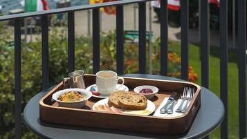 A balcony with a tray of breakfast items, flags, and a view of a body of water with mountains in the distance.