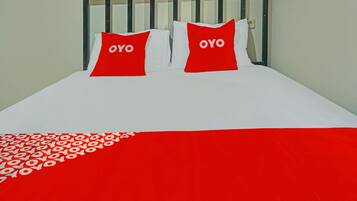 Ein Bett mit weißer und roter Bettdecke, zwei Kissen mit dem Schriftzug 'OYO' und ein schwarzes Metall-Kopfteil.
