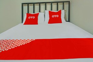 Un lit recouvert d’une couvre-lit blanche et rouge, deux oreillers ornés du mot « OYO », et une tête de lit en métal noir.