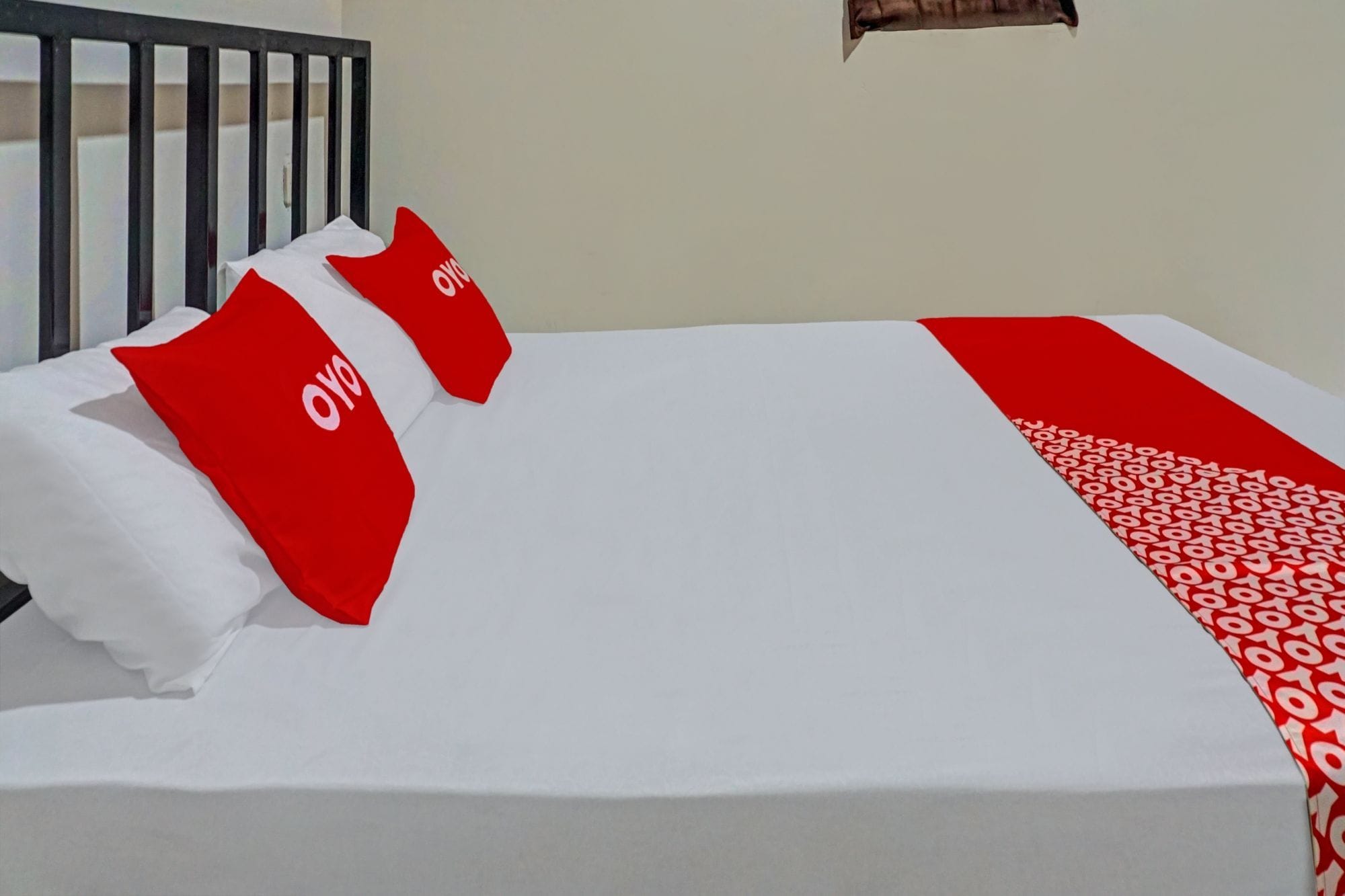 Uma cama com roupa de cama branca, almofadas vermelhas com um logotipo, cabeceira preta e manta estampada em vermelho e branco.