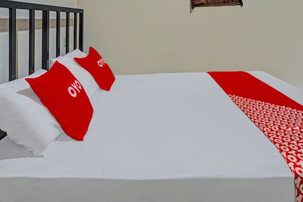 Uma cama com roupa de cama branca, almofadas vermelhas com um logotipo, cabeceira preta e manta estampada em vermelho e branco.