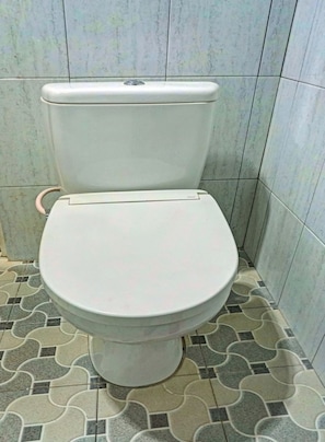 Sanitário com assento e caixa acoplada brancos, em frente a uma parede revestida com padrão geométrico.