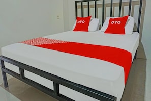 Ein Bett mit einer weißen Matratze, einer roten Decke und zwei Kissen mit dem Schriftzug 'OYO'.