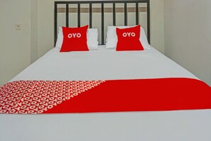 Una cama con cubrecama blanco y rojo, dos almohadas con el texto 'OYO' y un cabecero de metal negro.
