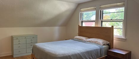 Une chambre à coucher avec un lit en bois, une table de chevet, une commode et une fenêtre avec des stores.