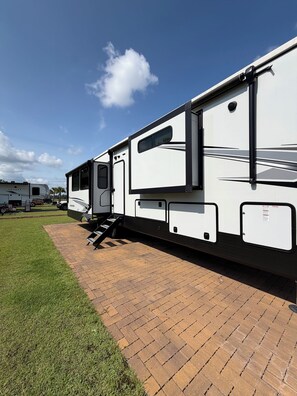 A white RV with a ramp leading to a covered area, parked on a paved driveway. - Luxury glamping suite near beaches & OWA, POOL! (Foley)