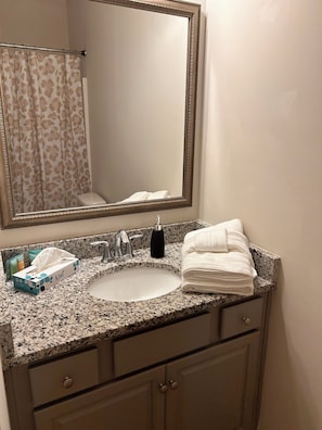 Une salle de bain avec un comptoir en granit, un lavabo, un miroir, un porte-serviettes et un rideau de douche.