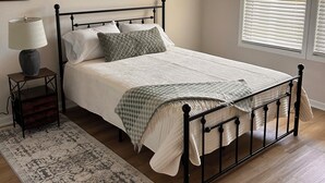 Un dormitorio con cama, mesita de noche, lámpara y una alfombra estampada.