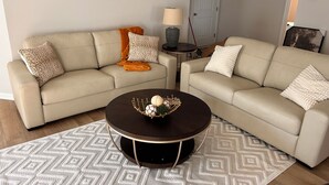 Una sala de estar con dos sofás color beige, una mesa de centro redonda oscura y alfombras con diseños.