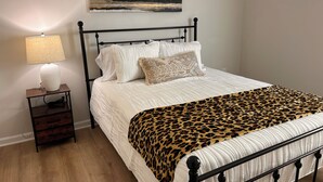 Una cama con una colcha de estampado de leopardo, una lámpara de noche y un cuadro en la pared.