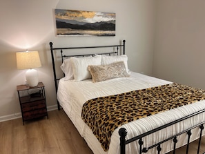 Un lit recouvert d’une couvre-lit à motifs léopard, une lampe de chevet et un tableau accroché au mur.