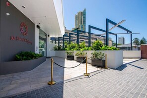 A modern building entrance with a clear sky, a sign reading 'We Don't Do Ordinary,' and a gated area with potted plants. - Dreamy Sands 1 Bedroom Coastal Escape (Surfers Paradise)