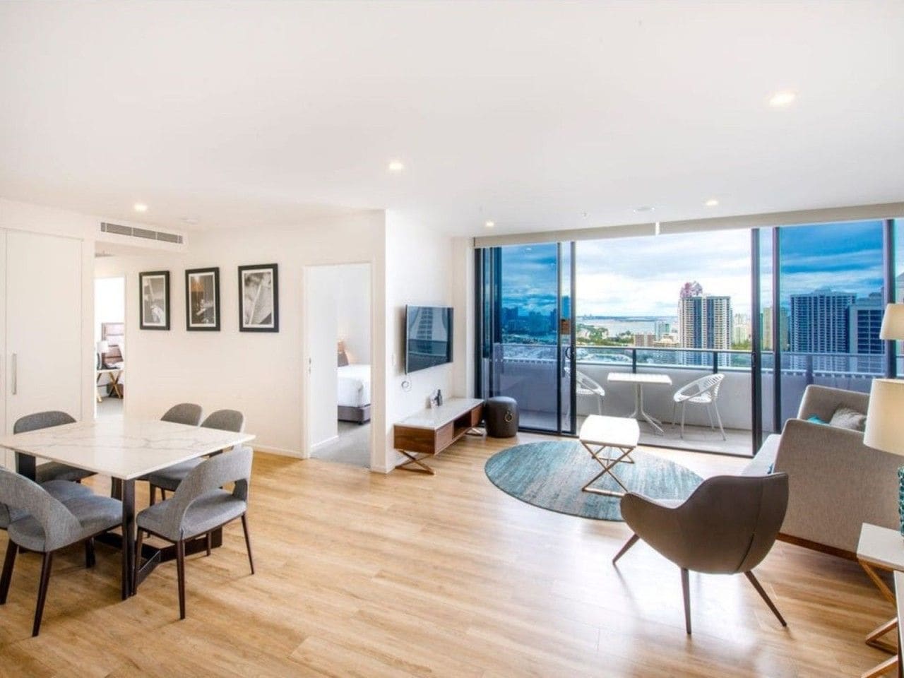 A modern living room with a dining area, large windows, and a city view.