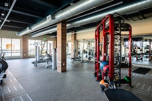 A gym with various exercise equipment, including a red Smith machine and weightlifting stations. - Spacious 2BD Apartment Home in the Heart of the OC (Santa Ana)