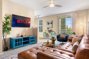 A living room with a leather sofa, a blue cabinet, a television displaying 'NETFLIX', and a large window. - Spacious 2BD Apartment Home in the Heart of the OC (Santa Ana)