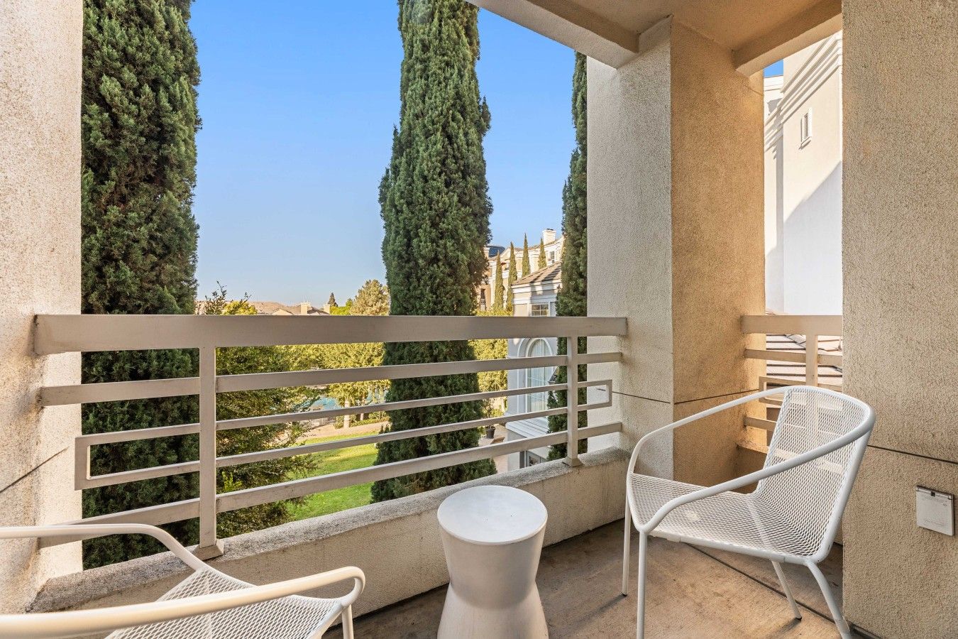 A balcony with a white metal railing, two white wicker chairs, and a small round table.