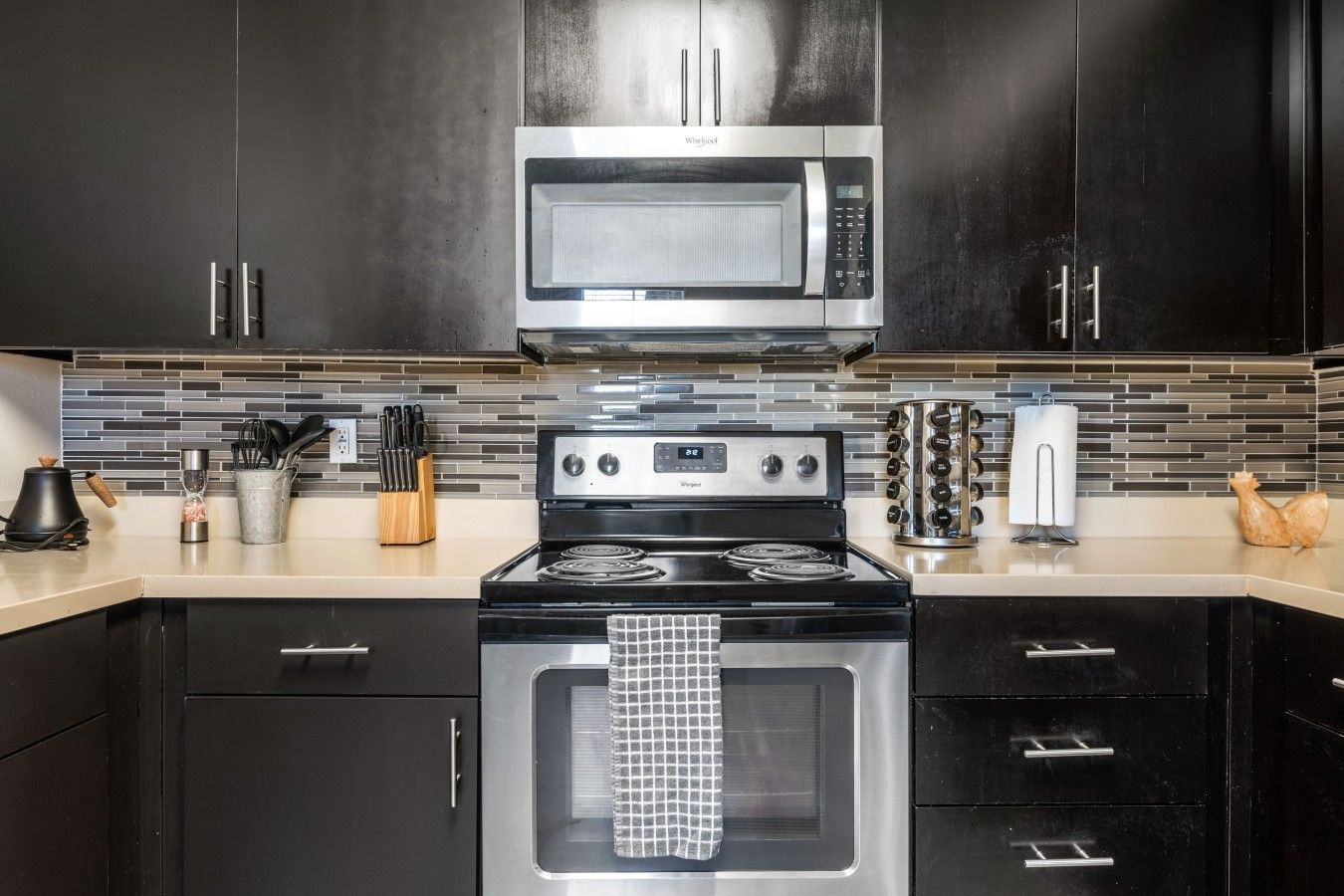 A modern kitchen with black cabinets, a stainless steel microwave, a gas stove, and a tiled backsplash.