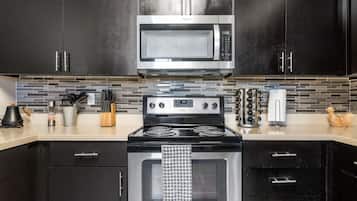 A modern kitchen with black cabinets, a stainless steel microwave, a gas stove, and a tiled backsplash.