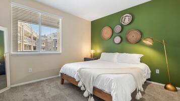 A bedroom with a bed, a window with blinds, a wall with decorative plates, and a floor lamp.