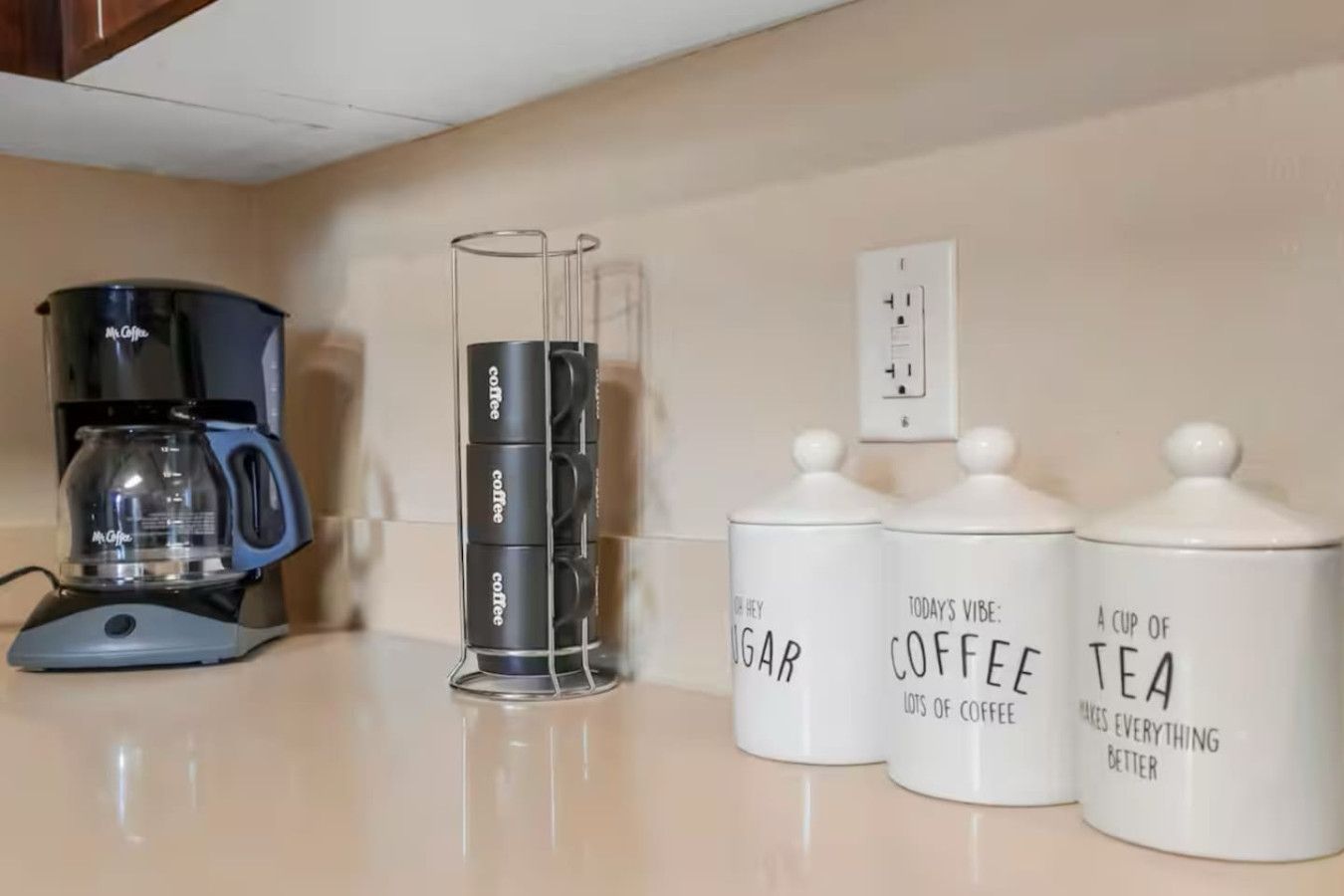 A kitchen counter with a coffee maker, a coffee grinder, and two containers labeled 'Today's vibe: coffee' and 'A cup of tea makes everything better.'