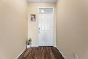 A hallway with a white door, beige walls, and a wooden floor. - Spacious 2BD Apartment Home in the Heart of the OC (Santa Ana)
