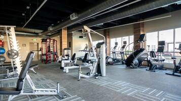 A gym with various exercise equipment, including treadmills and weight machines, and large windows providing natural light.