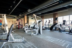 Une salle de sport équipée de divers appareils d’exercice, notamment des tapis de course et des appareils de musculation, et dotée de grandes fenêtres laissant entrer la lumière naturelle.
