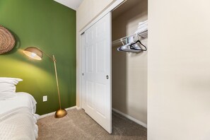A bedroom with a bed, a bedside lamp, a closet with hanging clothes, and a door. - Spacious 2BD Apartment Home in the Heart of the OC (Santa Ana)