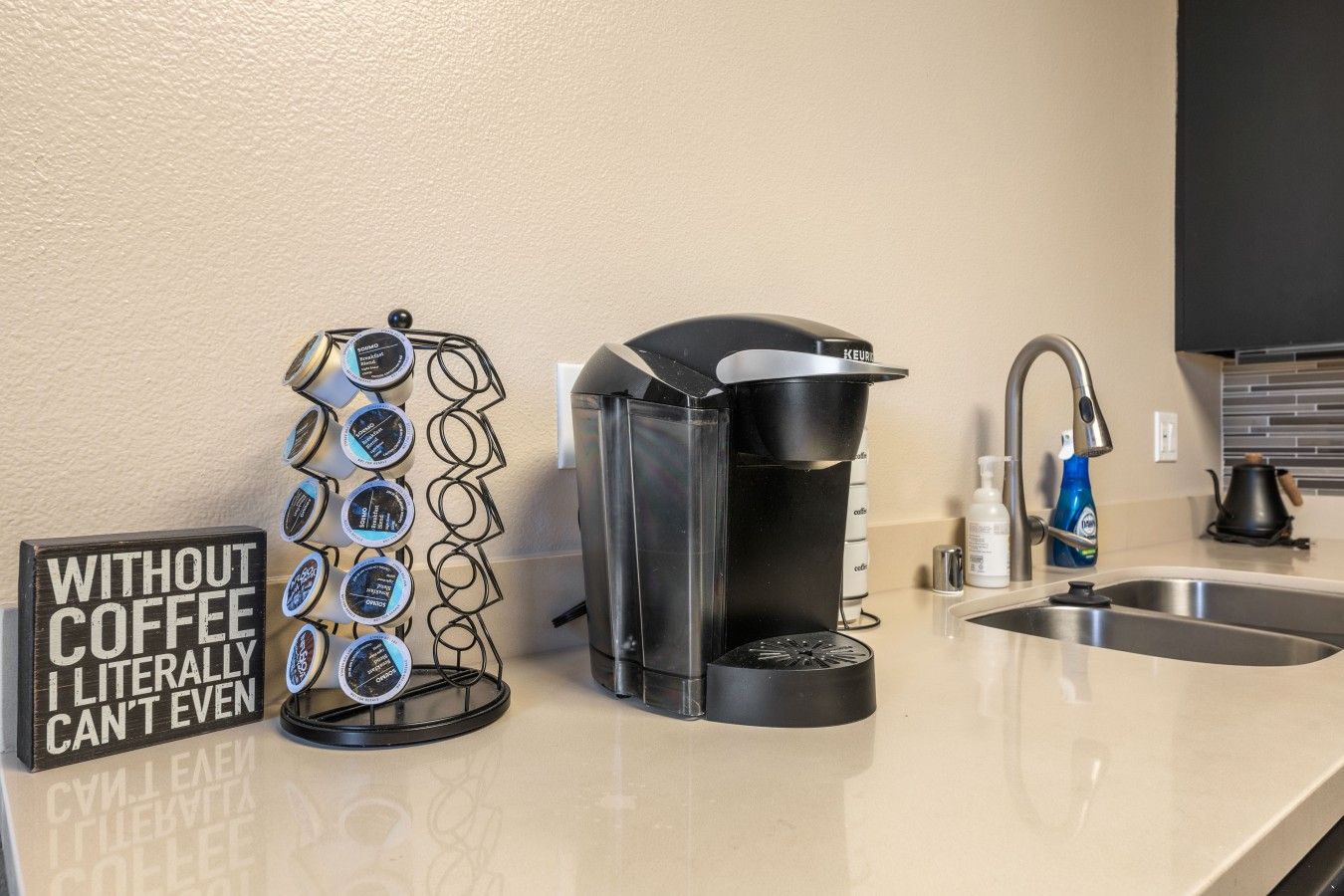 Une machine à café, un support pour dosettes de café et un panneau sur un comptoir de cuisine.